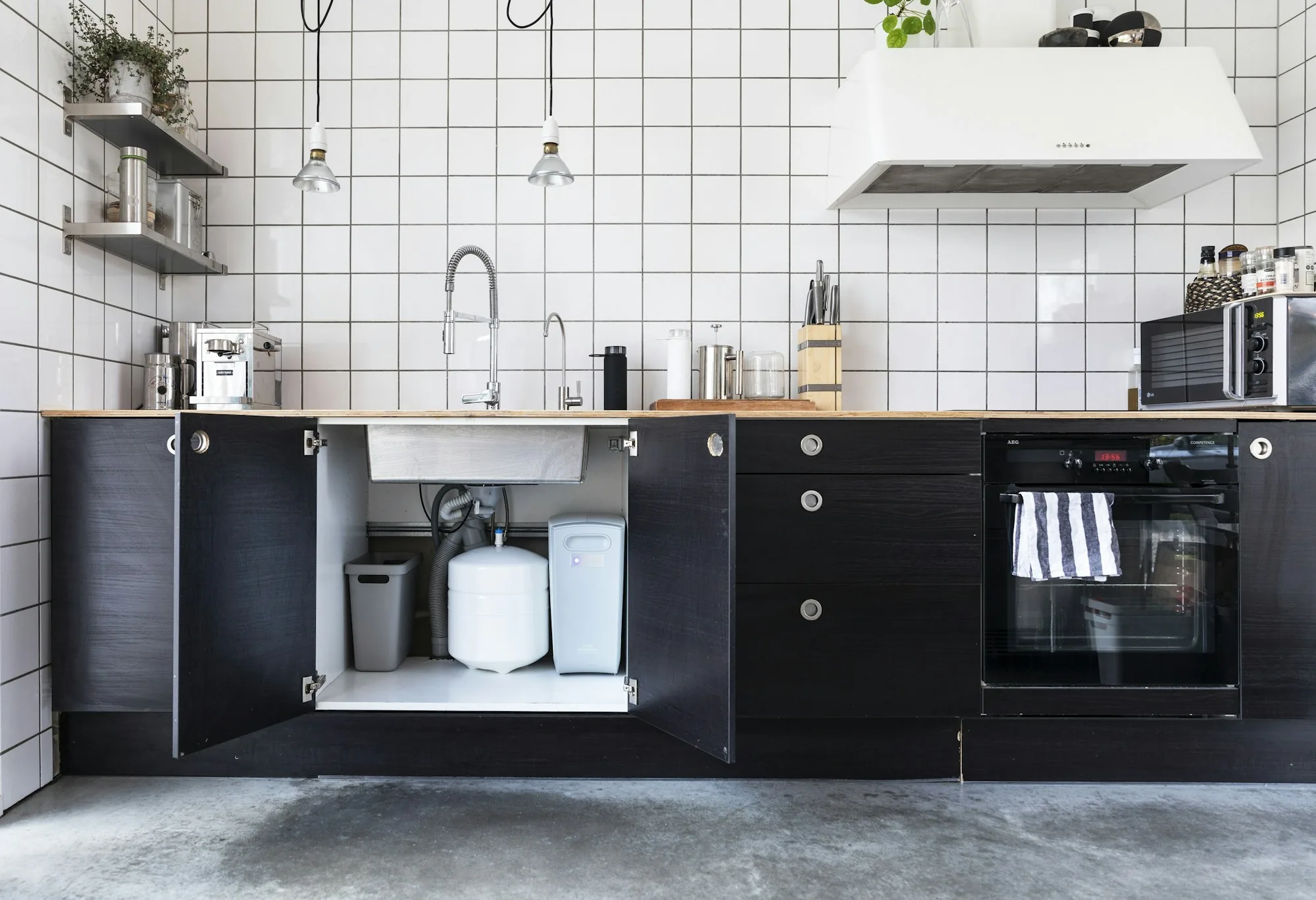 Under-sink drinking water filter with cartridge housings mounted inside a kitchen cabinet beside the supply lines